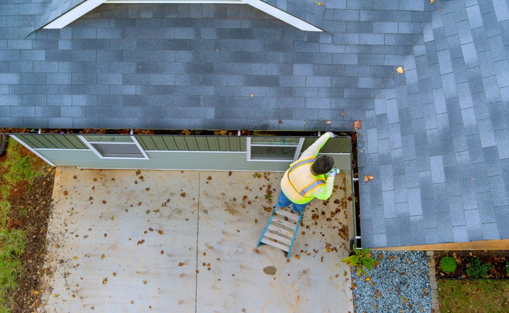 An employee is cleaning clogged roof gutter drain with dirt, debris, fallen leaves