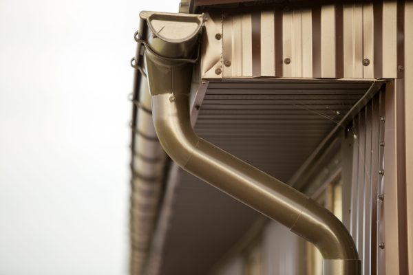 Close-up detail of cottage house corner with metal planks siding and roof with steel gutter rain system. Durability, professional construction, drainage pipes installation and connection concept.